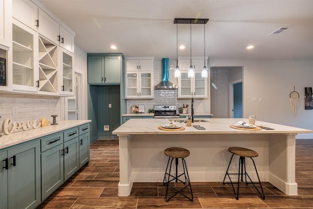 kitchen featuring white cabinetry, electric range, wall chimney range hood, an island with sink, and pendant lighting