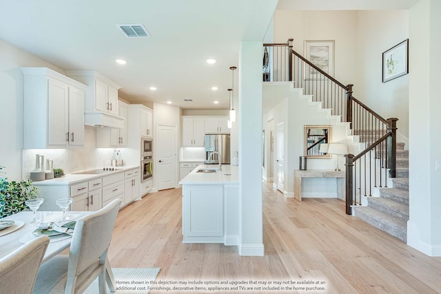 kitchen with appliances with stainless steel finishes, pendant lighting, decorative backsplash, white cabinets, and light wood-type flooring