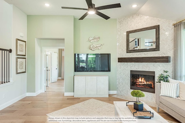 living room featuring a tiled fireplace, ceiling fan, light hardwood / wood-style flooring, and lofted ceiling