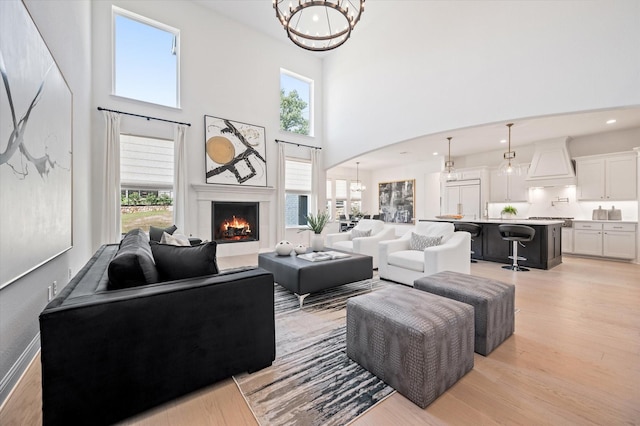 living room with a towering ceiling, a chandelier, and light wood-type flooring