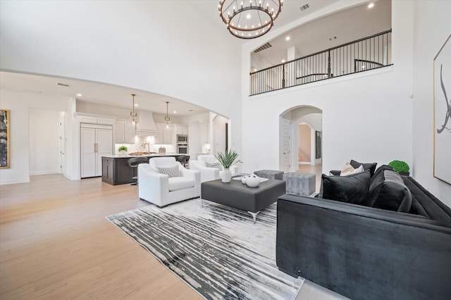 living room featuring sink, a towering ceiling, light hardwood / wood-style flooring, and a chandelier