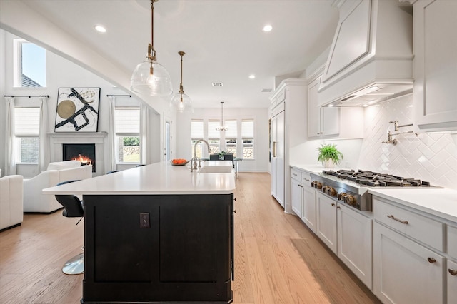 kitchen with a kitchen island with sink, sink, decorative backsplash, white cabinetry, and stainless steel gas cooktop