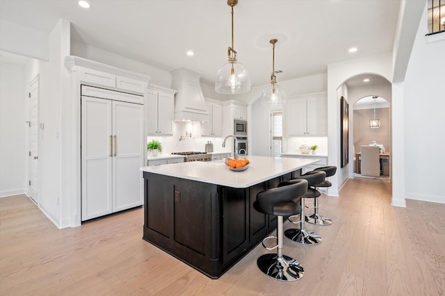 kitchen featuring white cabinetry, hanging light fixtures, built in appliances, a spacious island, and custom exhaust hood