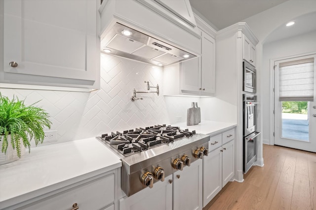 kitchen featuring appliances with stainless steel finishes, white cabinets, light wood-type flooring, and custom exhaust hood