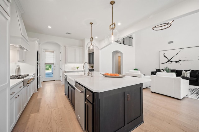 kitchen with stainless steel appliances, sink, decorative light fixtures, white cabinets, and an island with sink