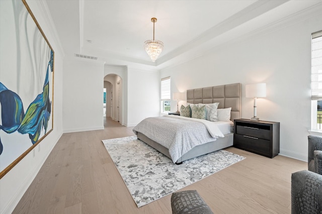 bedroom featuring a notable chandelier, light hardwood / wood-style floors, a raised ceiling, and crown molding