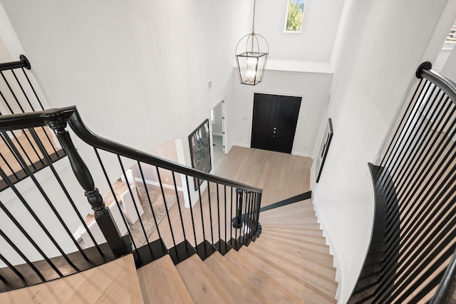 stairway featuring wood-type flooring, a high ceiling, and an inviting chandelier