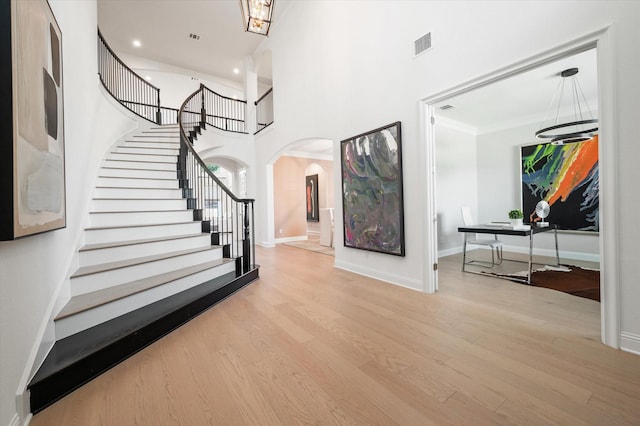 entryway featuring light wood-type flooring, ornamental molding, a high ceiling, and a chandelier