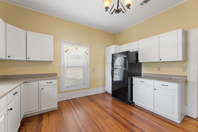 kitchen featuring hardwood / wood-style flooring, an inviting chandelier, white cabinets, and black refrigerator