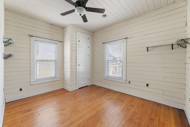 unfurnished bedroom with ceiling fan, light hardwood / wood-style floors, multiple windows, and wooden walls