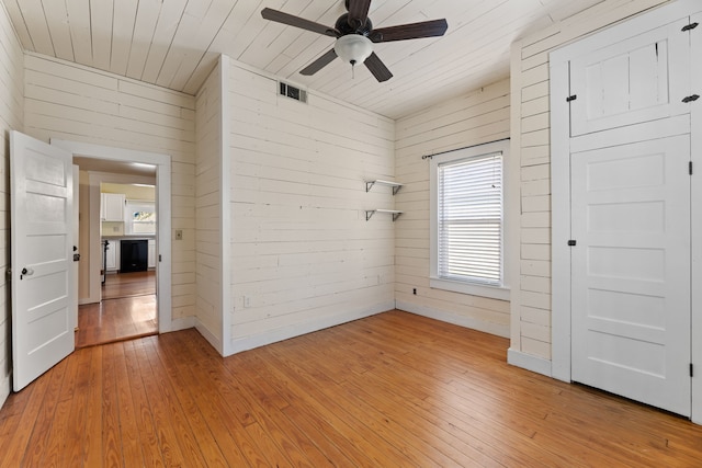 spare room featuring ceiling fan, wood walls, and light wood-type flooring