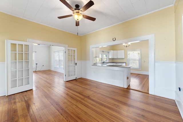 unfurnished living room featuring french doors, ceiling fan with notable chandelier, ornamental molding, and hardwood / wood-style flooring