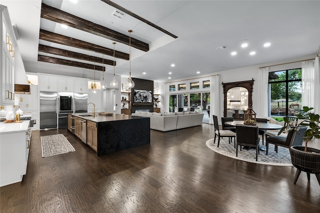 kitchen with beam ceiling, white cabinetry, sink, an island with sink, and decorative light fixtures