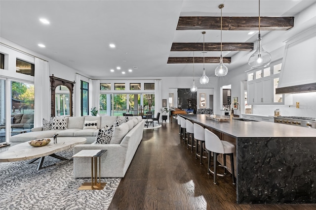 living room featuring dark wood-type flooring, sink, beamed ceiling, and a healthy amount of sunlight