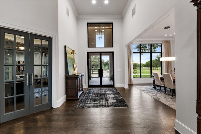 foyer entrance with dark hardwood / wood-style floors, a towering ceiling, ornamental molding, and french doors