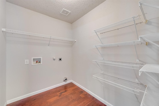 clothes washing area with a textured ceiling, hardwood / wood-style floors, electric dryer hookup, hookup for a washing machine, and gas dryer hookup