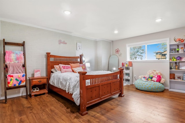 bedroom featuring wood-type flooring and brick wall