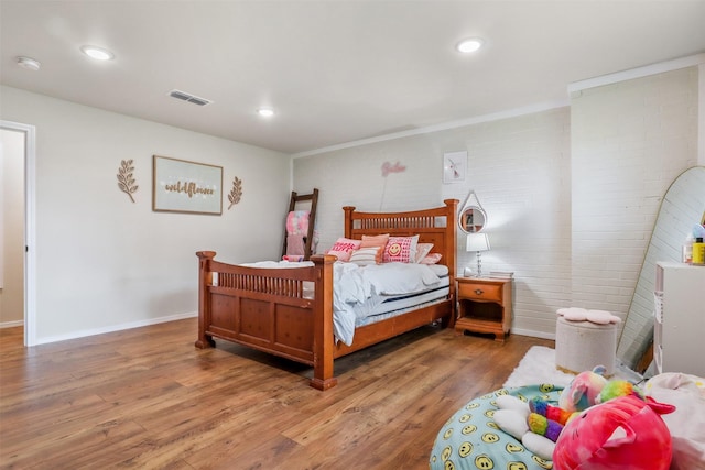 bedroom featuring wood-type flooring and brick wall