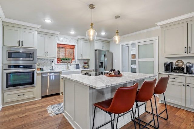 kitchen with light stone counters, ornamental molding, stainless steel appliances, light hardwood / wood-style floors, and a kitchen island