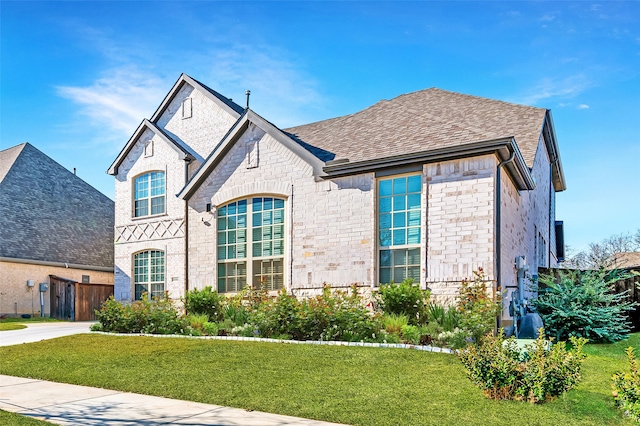 french country inspired facade featuring stone siding, a front lawn, and a shingled roof