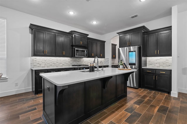 kitchen featuring sink, decorative backsplash, an island with sink, appliances with stainless steel finishes, and a kitchen bar