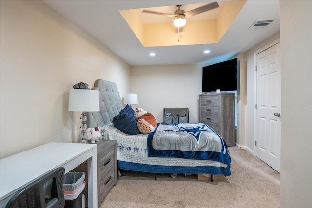 carpeted bedroom with ceiling fan and a raised ceiling