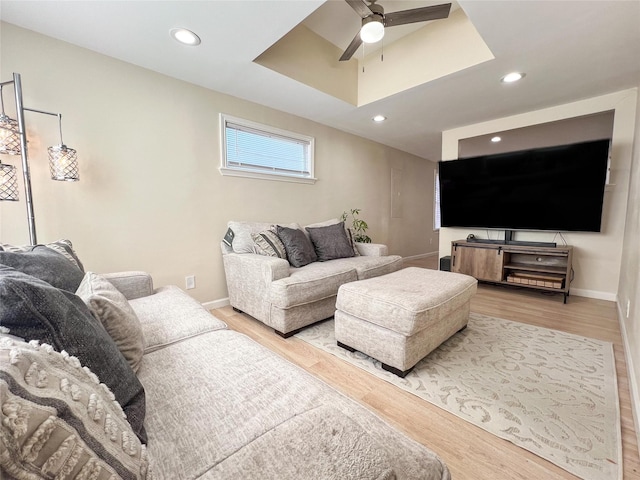 living room featuring light hardwood / wood-style floors, a raised ceiling, and ceiling fan