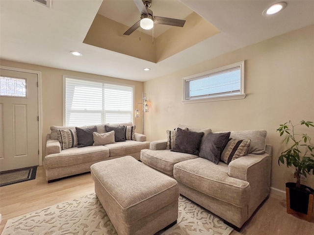 living room featuring ceiling fan, light hardwood / wood-style floors, and a tray ceiling