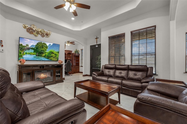 tiled living room with a raised ceiling and ceiling fan