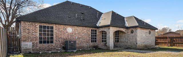 rear view of property with central air condition unit and a lawn