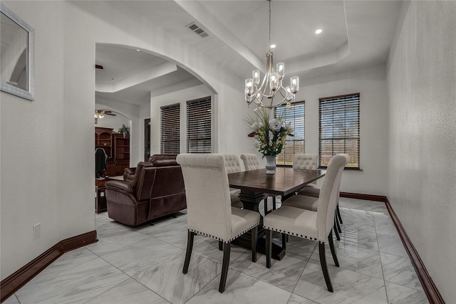 dining space featuring ceiling fan with notable chandelier and a tray ceiling