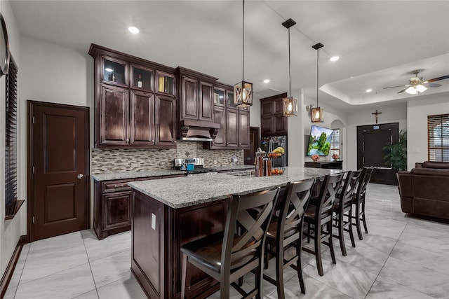 kitchen with dark brown cabinetry, ceiling fan, decorative light fixtures, stainless steel range oven, and an island with sink