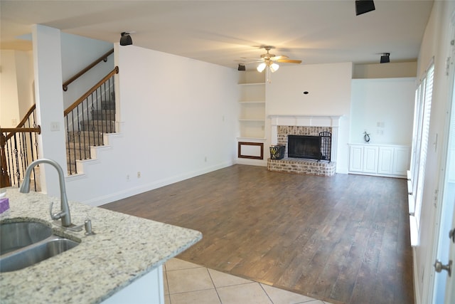 living room with ceiling fan, sink, built in features, a fireplace, and light tile patterned flooring