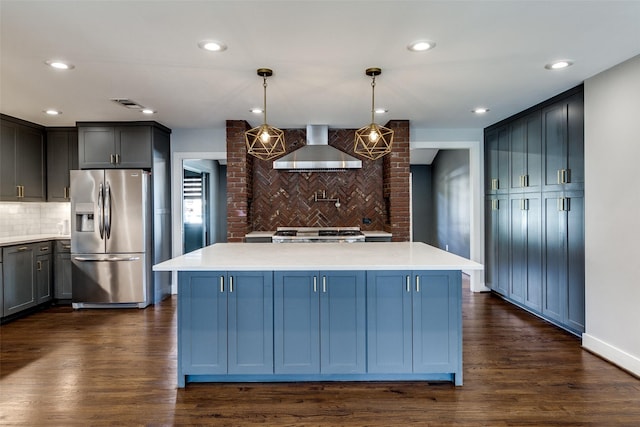 kitchen with a center island, backsplash, wall chimney range hood, hanging light fixtures, and stainless steel fridge