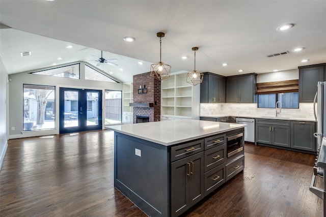 kitchen with gray cabinetry, stainless steel appliances, decorative light fixtures, a kitchen island, and lofted ceiling