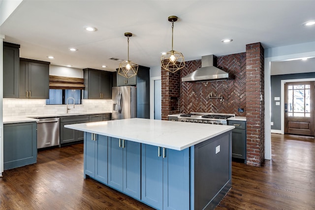 kitchen featuring backsplash, stainless steel appliances, wall chimney range hood, a kitchen island, and hanging light fixtures