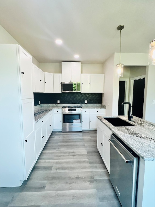 kitchen featuring white cabinetry, sink, stainless steel appliances, tasteful backsplash, and decorative light fixtures