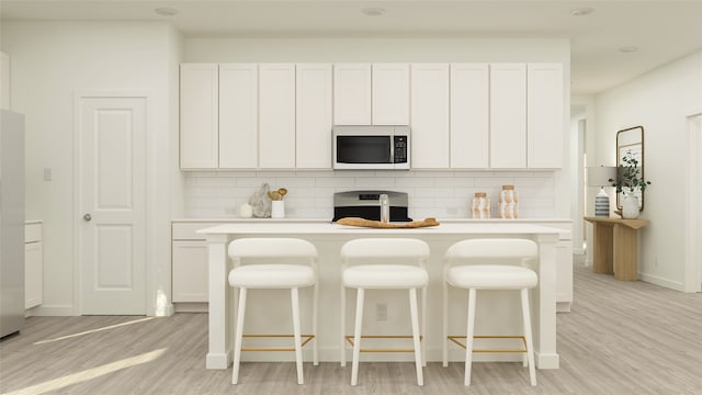 kitchen featuring a kitchen bar, white cabinetry, an island with sink, and light hardwood / wood-style floors