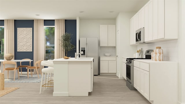 kitchen with a kitchen breakfast bar, backsplash, stainless steel appliances, a kitchen island with sink, and white cabinetry