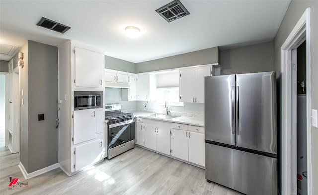 kitchen with backsplash, sink, light wood-type flooring, white cabinetry, and stainless steel appliances