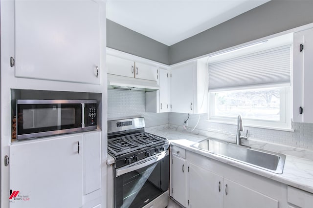 kitchen featuring sink, decorative backsplash, light stone countertops, appliances with stainless steel finishes, and white cabinetry