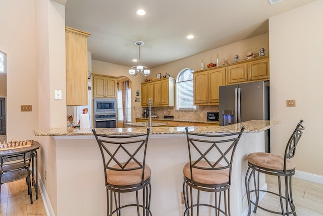 kitchen with appliances with stainless steel finishes, a kitchen breakfast bar, decorative backsplash, kitchen peninsula, and light hardwood / wood-style flooring