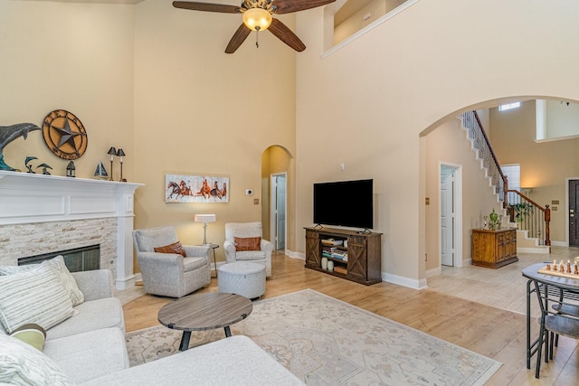 living room with a stone fireplace, light hardwood / wood-style floors, ceiling fan, and a high ceiling