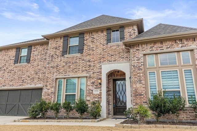 view of front of house featuring a shingled roof, concrete driveway, brick siding, and an attached garage