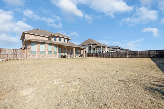 rear view of property featuring brick siding, a yard, and a fenced backyard