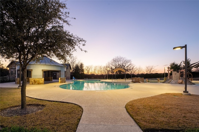 pool at dusk with an outbuilding, a patio area, an exterior structure, and an outdoor pool