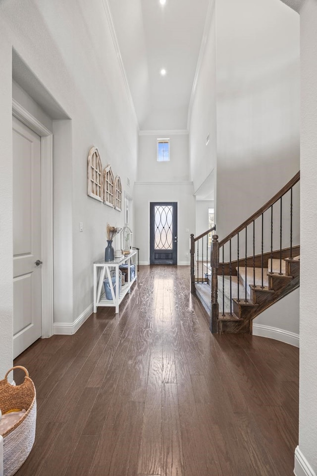 entrance foyer with hardwood / wood-style flooring, a towering ceiling, ornamental molding, baseboards, and stairs