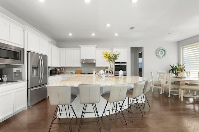 kitchen featuring tasteful backsplash, dark wood-style floors, appliances with stainless steel finishes, a kitchen breakfast bar, and under cabinet range hood