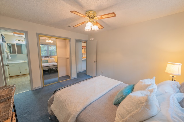 bedroom featuring a textured ceiling, ceiling fan, dark carpet, and ensuite bathroom