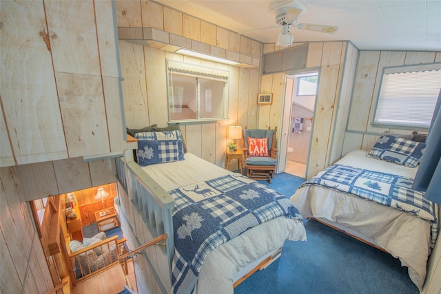 carpeted bedroom with ensuite bath, ceiling fan, and wooden walls